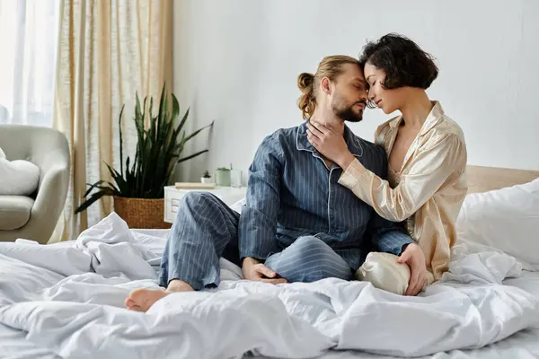A loving couple in pajamas cuddles on a white bed. — Stock Photo