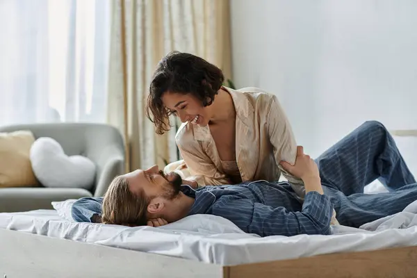 Couple in bedroom shares tender moment, woman sitting on bed, man lying down looking lovingly. — Stock Photo