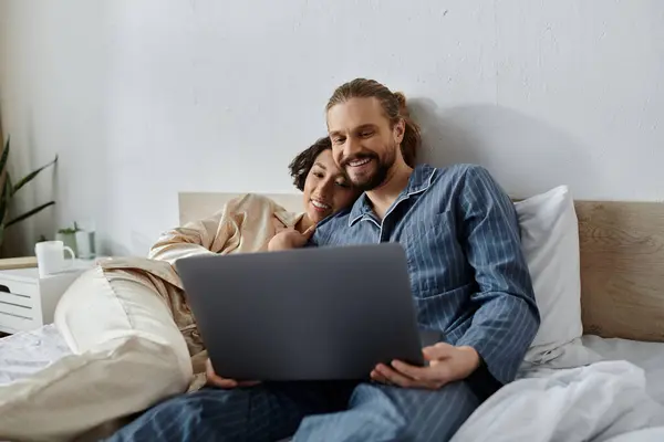 A loving couple relaxes in bed together, watching a laptop. — Stock Photo