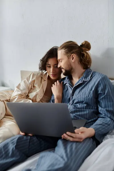 A loving couple cuddles in bed while browsing on a laptop. — Stock Photo