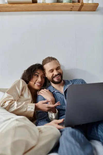 A loving couple cuddles on the couch while watching a movie on their laptop. — Stock Photo