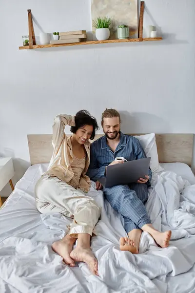A couple relaxes in bed, using a laptop and enjoying each others company. — Stock Photo