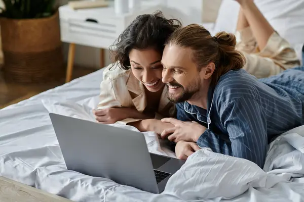 A couple is lying on a bed, looking at a laptop and smiling. — Stock Photo