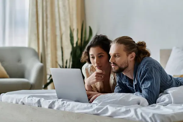 A young couple lies on a bed, looking at a laptop together. — Stock Photo