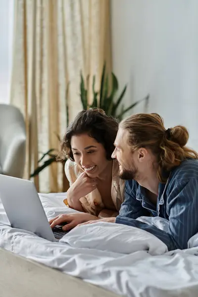 A loving couple spends time together at home, relaxing in bed and browsing the internet on a laptop. — Stock Photo
