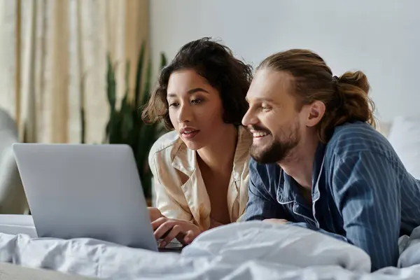 A loving couple relaxing together on a bed, browsing a laptop. — Stock Photo