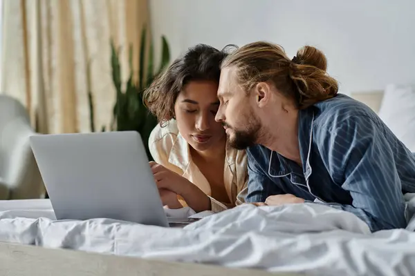 Um casal aconchega-se na cama, olhando para um laptop. — Fotografia de Stock