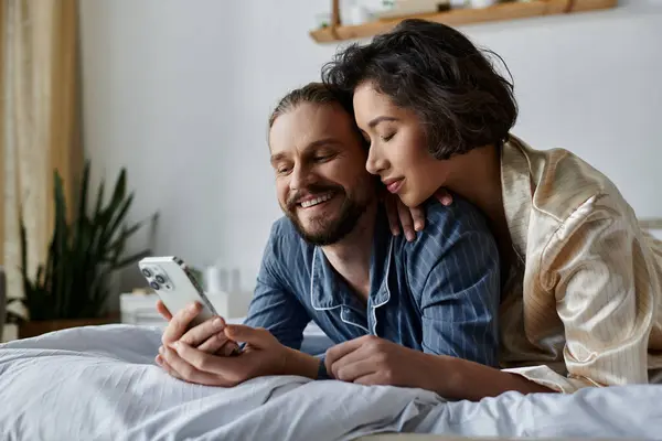 Couple in bed: man on phone, woman resting on his shoulder. — Stock Photo