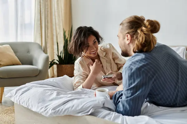 A couple relaxes on their bed, enjoying a cup of coffee and a conversation. — Stock Photo