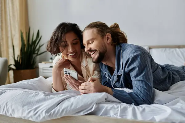 A couple relaxes in bed, sharing a laugh and a phone. — Stock Photo