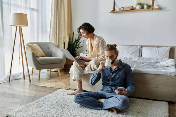 A couple enjoys a relaxed morning at home, one working on a laptop, the other sipping coffee. — Stock Photo