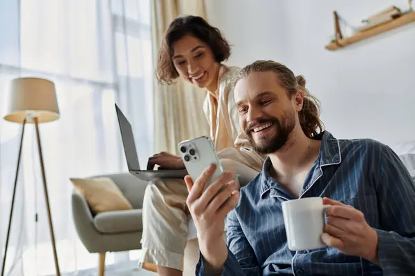 A loving couple relaxing at home, enjoying coffee and using technology. — Stock Photo