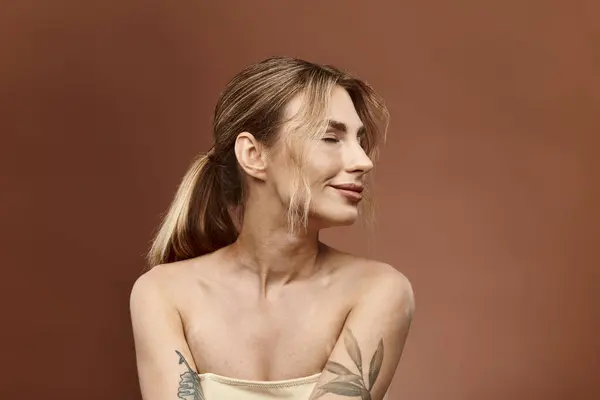 A young woman with vitiligo and a tattoo on her arm poses with her shoulders bare against a beige background. — Stock Photo
