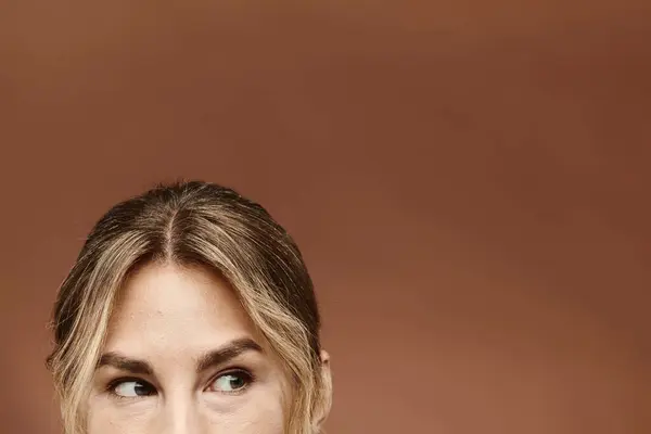 Una joven confiada mira fuera de cámara sobre un cálido telón de fondo beige. - foto de stock