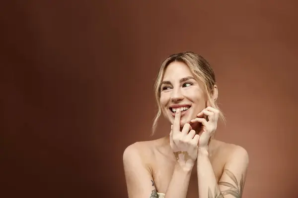 A young woman with vitiligo and a tattoo on her arm smiles while posing with bare shoulders against a beige background. — Stock Photo