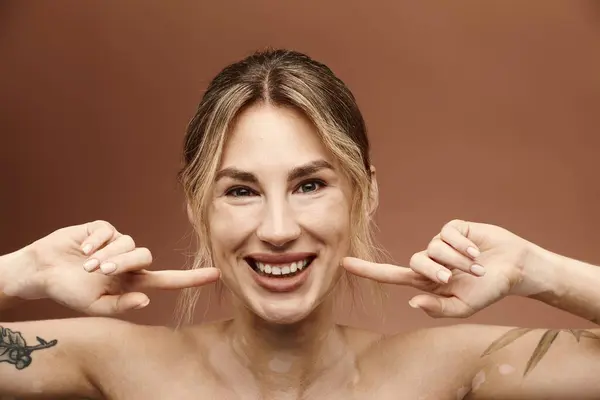 A young woman with vitiligo and a tattoo smiles while posing with her shoulders bare against a beige background. — Stock Photo