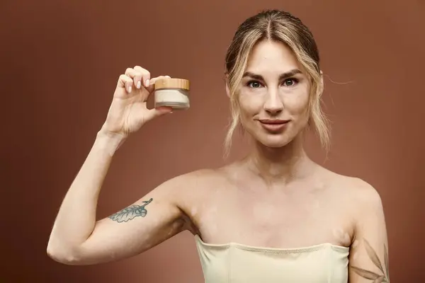 Una joven con vitiligo sostiene un frasco de crema, mostrando su confianza y compromiso con el cuidado de la piel. - foto de stock