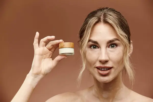 A young woman with vitiligo holds a cream jar in front of her face against a beige background. She smiles confidently. — Stock Photo