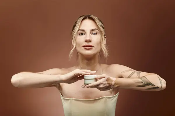 Una joven con vitiligo sostiene un frasco de crema frente a ella, mirando directamente a la cámara. — Stock Photo