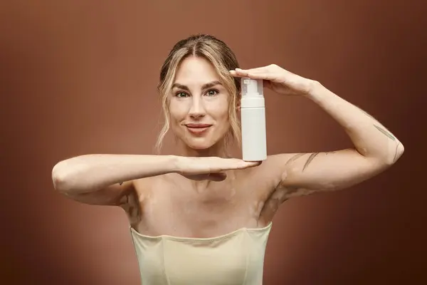 A young woman with vitiligo holds a skin care product in front of a beige background. — Stock Photo