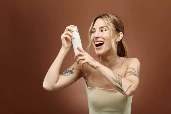 A young woman with vitiligo smiles while holding a skin care product in front of a beige background. — Stock Photo