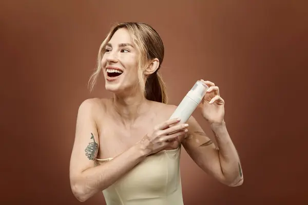 Une jeune femme avec des sourires de vitiligo tout en tenant un produit de soins de la peau devant un fond beige. — Photo de stock