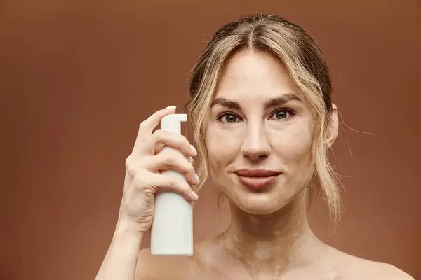 A young woman with vitiligo holds a skincare product in front of a beige background. — Stock Photo