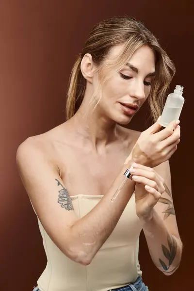 Una joven con vitiligo sostiene un producto para el cuidado de la piel y se lo aplica en el brazo. - foto de stock