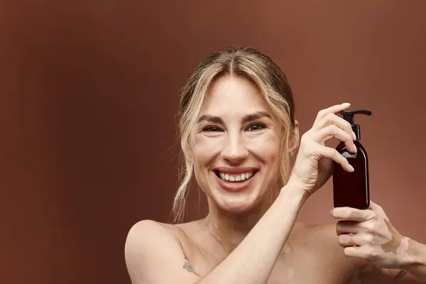 Eine junge Frau mit Vitiligo lächelt strahlend, als sie eine Flasche Hautpflegeprodukt vor beigem Hintergrund hält. — Stockfoto