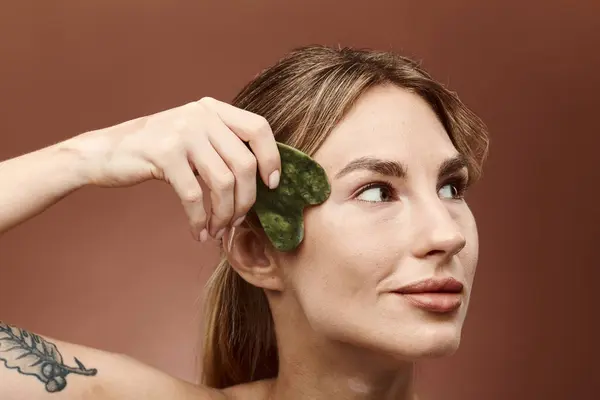 A young woman with vitiligo uses a jade stone on her face for a skincare routine. — Stock Photo