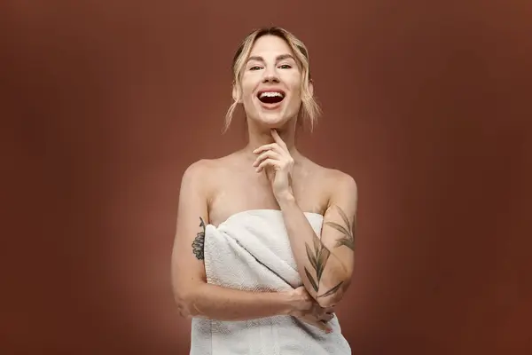 Une jeune femme au vitiligo se tient enveloppée dans une serviette, souriante et confiante. Le fond beige souligne sa beauté naturelle. — Photo de stock