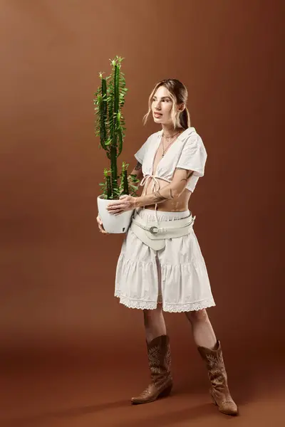 Giovane donna in bianco abbigliamento estivo in posa con un cactus su uno sfondo beige. — Foto stock