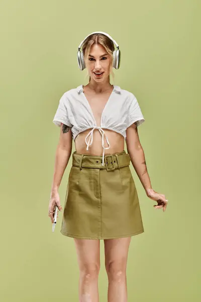 A young woman with vitiligo poses in a white top and olive green skirt, exuding confidence and style against a green backdrop. — Stock Photo
