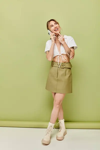 A young woman with vitiligo poses in a white summer outfit on a green backdrop. She is smiling and talking on her phone. — Stock Photo