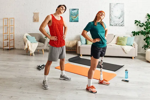 A woman with a prosthetic leg and her boyfriend stretch together on yoga mats in their living room. — Stock Photo