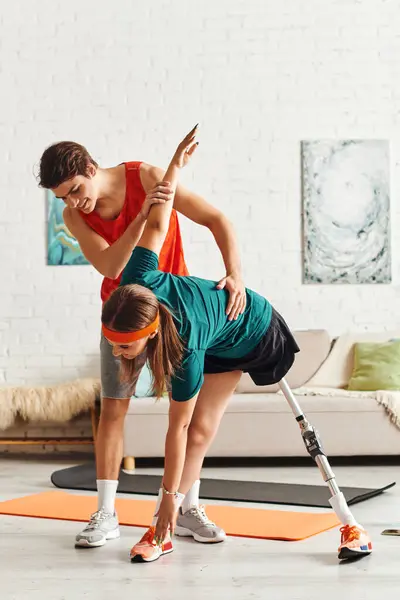 A woman with a prosthetic leg stretches while her boyfriend assists her. — Stock Photo