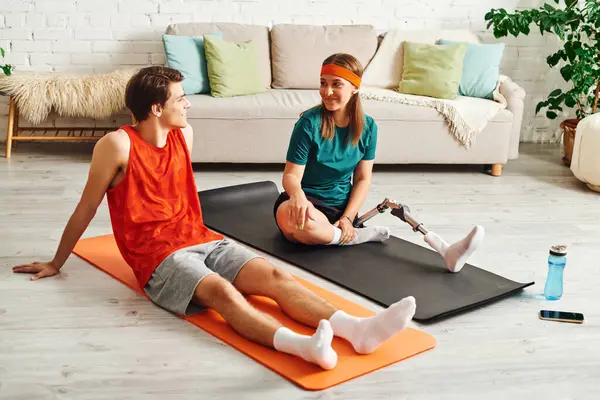 Una mujer con una pierna protésica y su novio practicando yoga sobre alfombras en casa. — Stock Photo