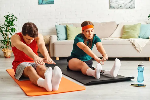 A woman with a prosthetic leg stretches on a yoga mat with her boyfriend. — Stock Photo