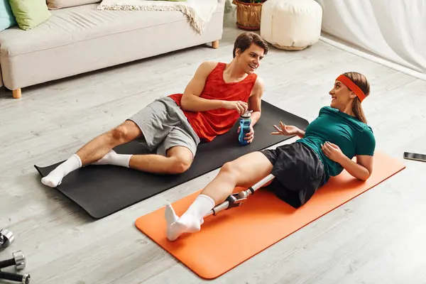Woman with prosthetic leg chats boyfriend on orange and black yoga mats. — Stock Photo
