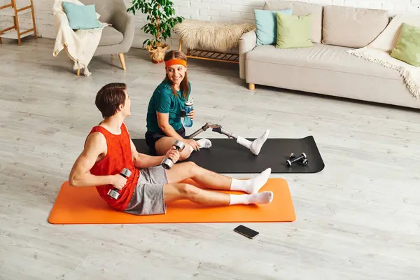 A couple exercises together in a living room. The woman has a prosthetic leg. — Stock Photo