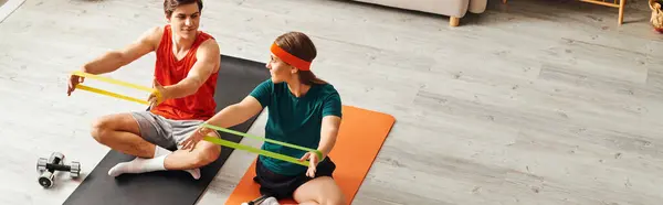 A woman with a prosthetic leg and her boyfriend work out together at home, using resistance bands. — Stock Photo