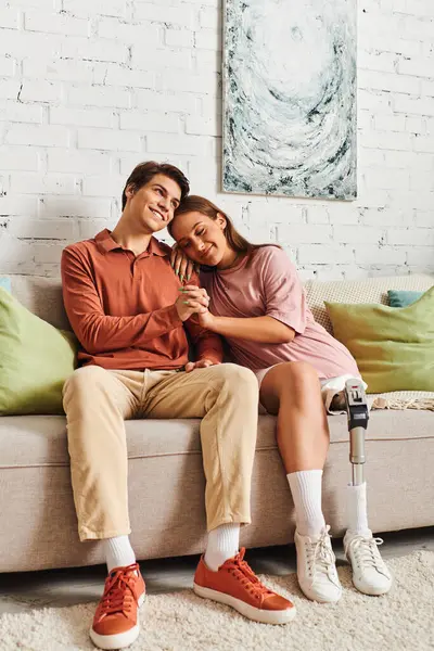 A young couple sits on a couch, the woman resting her head on her boyfriends shoulder. — Stock Photo