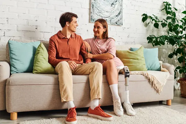 Young couple on couch gaze lovingly, woman has prosthetic leg. — Stock Photo