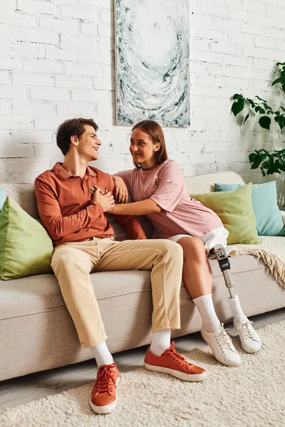 A couple, a woman with a prosthetic leg and her boyfriend, share a laugh while sitting on a couch. — Stock Photo