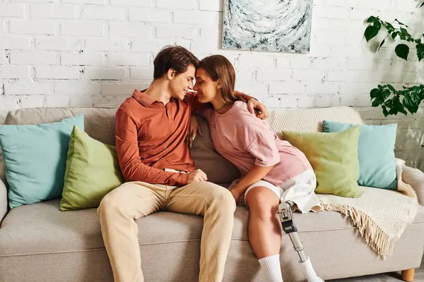 Eine Frau mit Beinprothese und ihr Freund teilen einen zärtlichen Moment auf einem Sofa. — Stockfoto