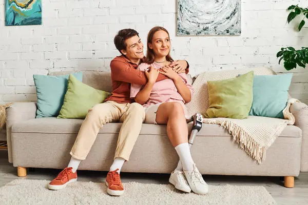 A woman with a prosthetic leg embraces her boyfriend while sitting on a couch. — Stock Photo