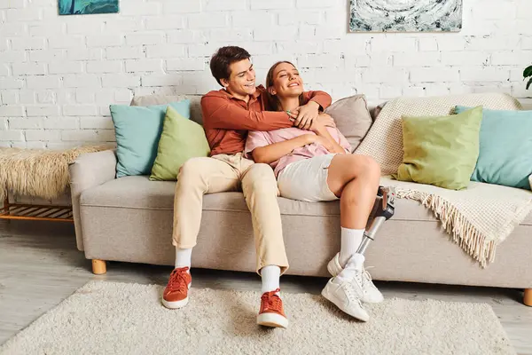 A couple sits on a couch, the woman wearing a prosthetic leg, with her boyfriend holding her close. — Stock Photo