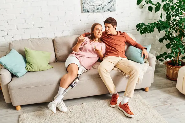 A couple sits on a couch together, the woman with a prosthetic leg. — Stock Photo