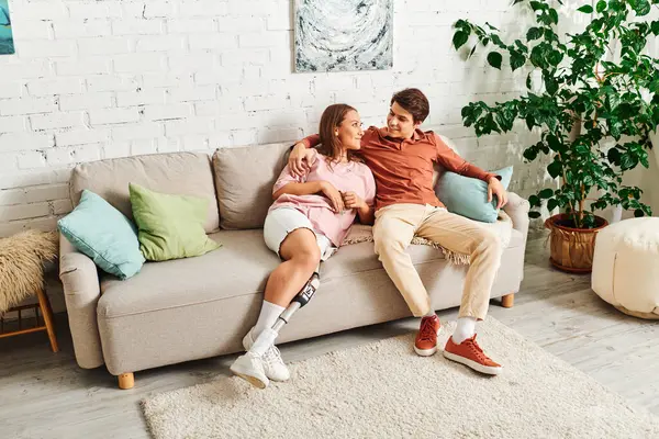 Woman with prosthetic leg smiles at boyfriend on couch. — Stock Photo