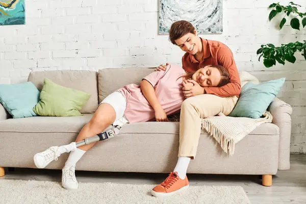 A woman with a prosthetic leg rests on the couch, laughing with her boyfriend. — Stock Photo